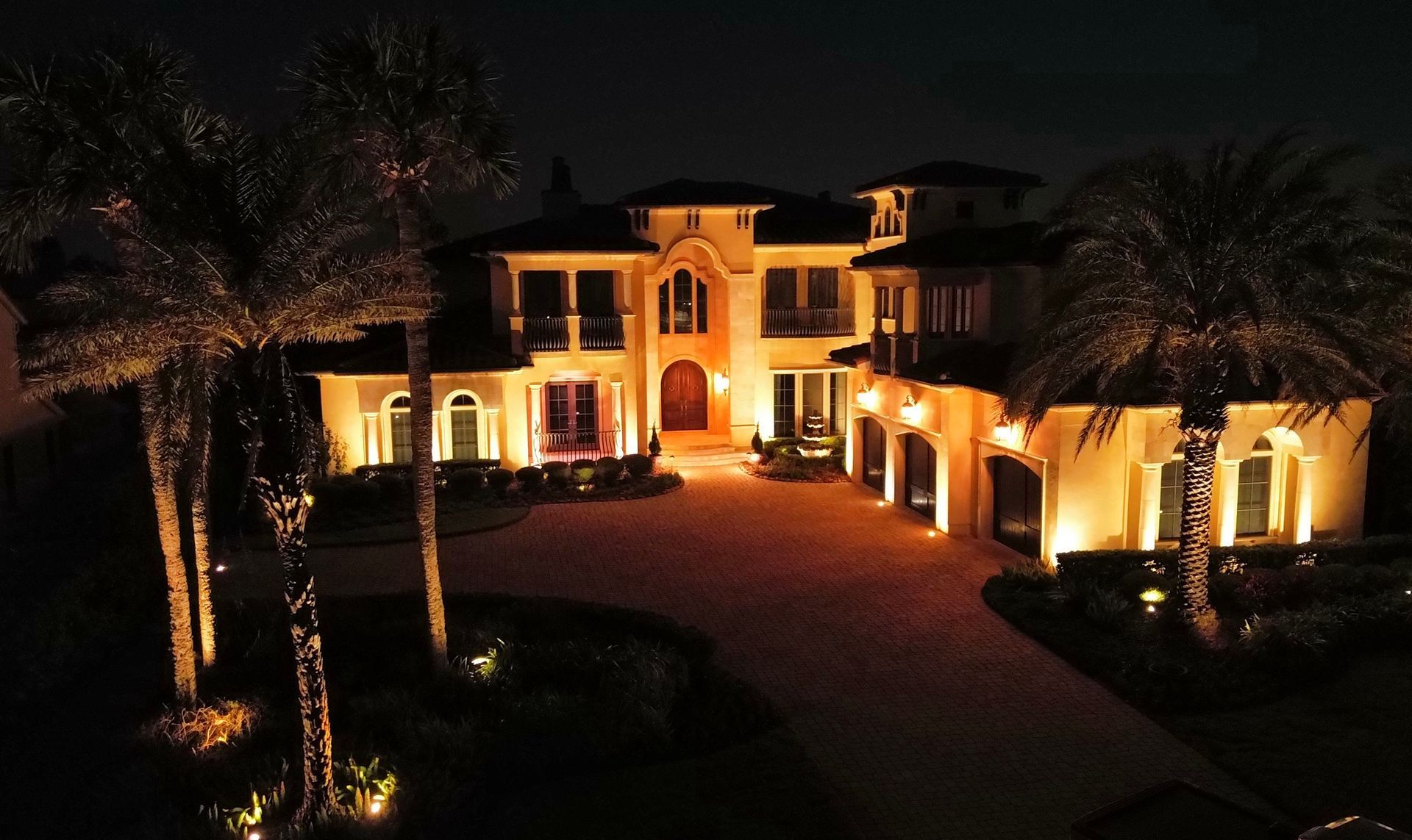 Aerial view of a Mediterranean-style Florida home with palm and architectural uplighting