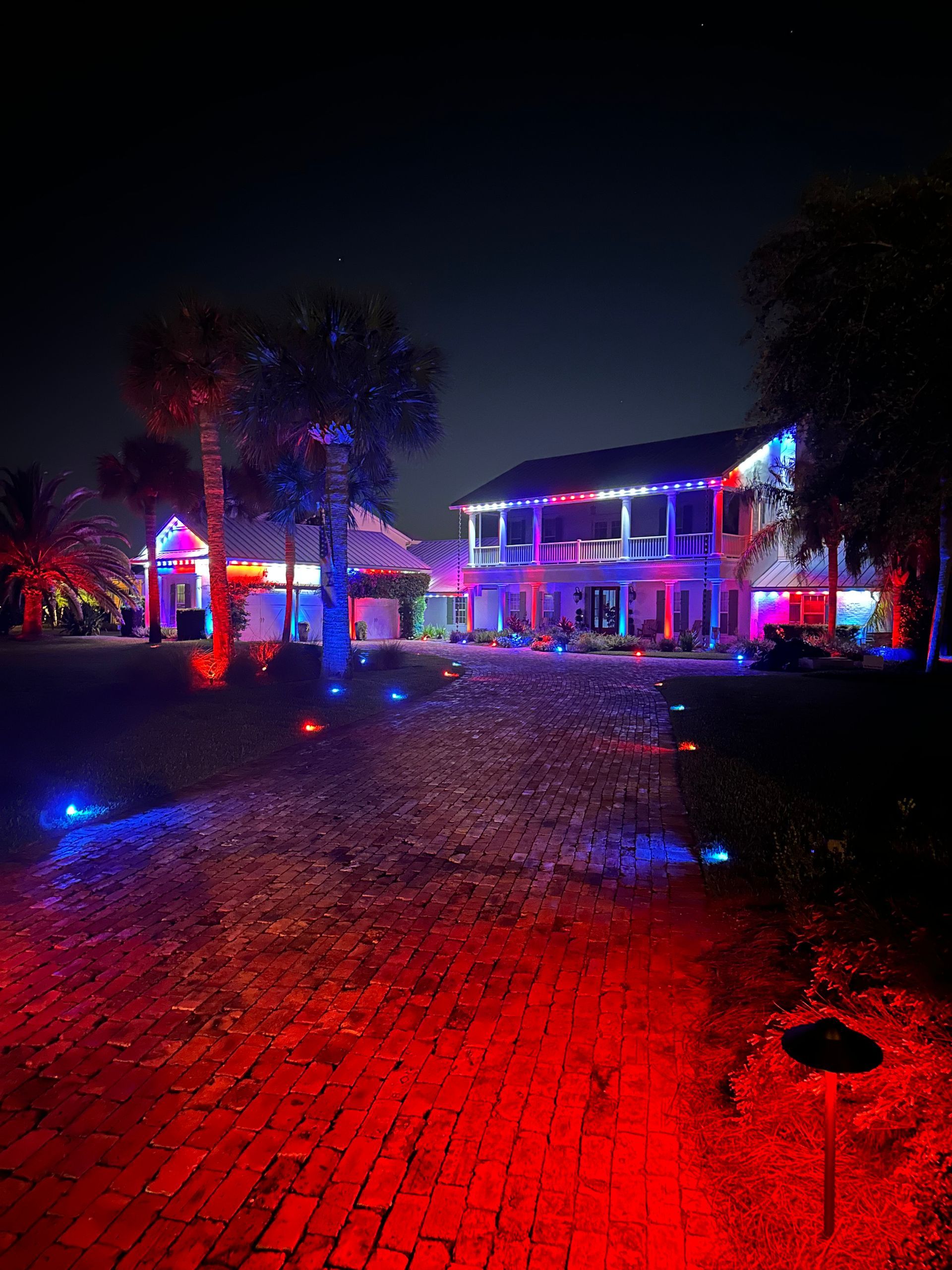 Large estate with red, white, and blue permanent lighting and palm uplighting